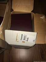 Top view of closed maroon folder inside a cardboard box