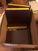 Top-down view of a cardboard box with four brown binders of National Geographic magazines inside.