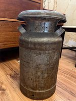 Front angle view of the metal milk can showing its cylindrical shape, handles, lid and surface wear.