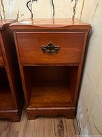 Front view of wood nightstand showing drawer with decorative handle and open shelf beneath.