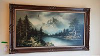 Full view of framed landscape painting featuring mountains, lake, and pine trees, signed by artist.