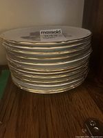 Stack of twelve white porcelain dessert plates with gold trim on scalloped edges.