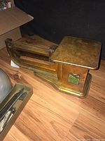 Front-side view of the vintage air mail scale showing the sliding scale arm and weighing platform on a wooden floor with a black background.