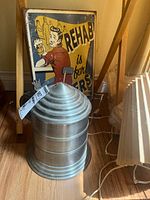 Photo showing the 10-inch metal beer stein with its lid and handle, positioned on a wooden floor near a wooden chair and a metal sign behind it.