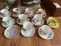 Overview photo of ten diverse vintage fine bone china teacups and saucers, showing variety of colors and patterns on wooden surface.