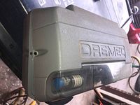 Closed gray plastic case with Dremel brand embossed, showing some accessories in see-through compartment.