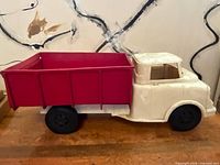 Side view of vintage toy dump truck showing white cab and red dump bed on wooden surface