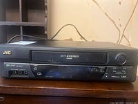 Front view of JVC VHS Hi-Fi VCR showing cassette slot, buttons, and logos including JVC and Hi-Fi Stereo.