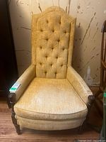 Front view of yellow vintage tufted arm chair showing full seat, armrests and tall backrest with button tufting.