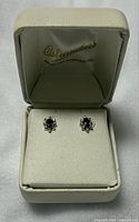 Pair of amethyst and diamond earrings displayed in original Ostranders cream-colored jewelry box with lid open