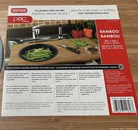 Box packaging showing brand Dexas popware, product name bamboo strainer board with measurements 12 in x 22 in, description of features including collapsible silicone strainer for space saving.