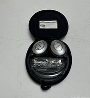 Bose QuietComfort 15 headphones folded in black zippered hard case with owner's guide inside lid, including audio cables still in plastic bag.