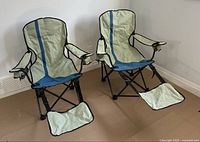 Two collapsible camping chairs with beige and blue fabric set up side by side, showing complete structure, fabric seats, armrests and footrests.