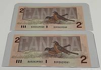 Back view of both 1986 Canadian 2 dollar bills showing illustration of robins and 'CANADA' text.