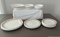 Set of dishes displayed on table including plates stacked by size and bowls arranged on white cloth riser showing gold floral butterfly border pattern.