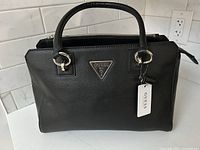 Front view of black Guess handbag with logo plaque and attached tag