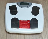 Top-down image of the Health O Meter digital scale showing four black sensor pads, a central digital display, control buttons, and a caution label on the surface.