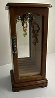 Front view of the wooden jewelry holder showing stained glass motif on the glass door and metal latch.