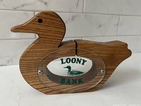 Front view of the solid oak bird-shaped bank labeled 'Loony Bank' with clear oval plaque featuring a loon illustration.