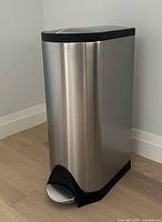 Front view of rectangular stainless steel trash can with black base and pedal foot step.