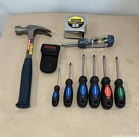 Top view of hammer, tape measure, six screwdrivers arranged side by side, and black pouch.