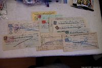 Photo showing 11 old bank cheques spread on a table with visible stamps and handwriting.