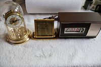 Three vintage desk clocks: Birks anniversary clock under glass dome, small wind-up gold-tone clock, and Seth Thomas Speed-Read flip clock