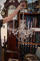 Person holding the chandelier by its chain showing the entire piece against a bookshelf background with a grandfather clock seen to the left.