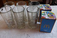 Six clear drinking glasses and two boxed McDonald's glasses displayed on white cloth