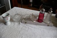 Complete lot displayed on white towel showing all items including stoneware and glass egg cups, sugar bowl, muffineers, dog candy holder and cake lifter box.