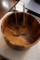 Top view of wooden salad bowl containing two wooden serving tongs with decorated handles.