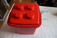 Red LEGO storage bin closed, showing top with four LEGO studs embossed with LEGO logos.