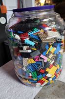 Large clear plastic container filled with assorted LEGO bricks and pieces of many colors visible through the container, with a purple lid on top.