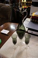 Full view of tall green glass cruet with stopper flanked by two matching green glasses on a cloth surface.