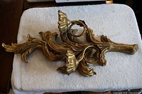 Pair of large decorative plaster wall candle sconces laid on a white towel, showing the detailed leaf and candle holder design, ornate gold finish.