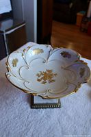 Top view of white porcelain fruit bowl decorated with gold floral motifs and gold trim on scalloped edges.