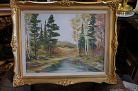 Frontal photo of the large oil painting in its ornate gold frame showing landscape with trees and water