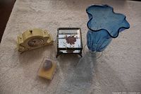 Small decor lot displayed on carpet including wind-up clock, French keepsake box with agate stone, blue glass vase, and inlaid jewel box.