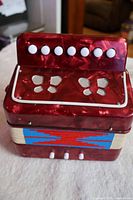 Front view of the small red marbled accordion showing eight white keyboard buttons and silver grille decoration.