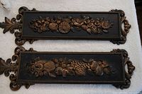 Close-up of two Syroco wall plaques featuring carved floral and fruit designs with ornate edges and finials.