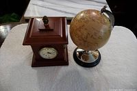Photo showing wooden weather station and small globe on chrome and wood stand together on white fabric background.