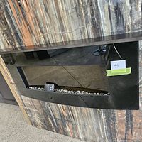 Close view of black glass fireplace insert mounted in display panel with decorative stones