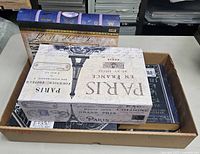 Set of 3 Paris themed decorative storage books and Paris styled storage box in a tray on a tabletop, showcasing the sizes and top surfaces.