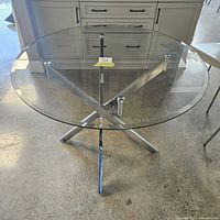 Full front view of the round glass top table with chrome metal base in showroom setting.