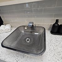 Installed square glass vessel sink on countertop with faucet and soap dispenser visible