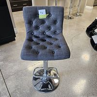 Front view of grey fabric tufted bar stool showing seat and chrome base.