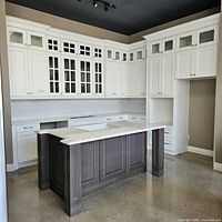 Front view of painted white Shaker wall and base cabinets with grey stained island and quartz countertop