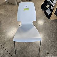 Front-facing view of a white molded chair with chrome metal legs on a concrete floor.
