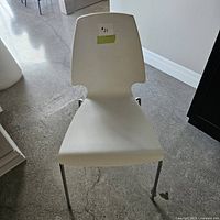 Front view of a white chair with chrome legs on a concrete floor showing shape and condition.