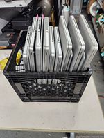 Milk crate holding eleven Apple laptops stacked vertically showing port sides